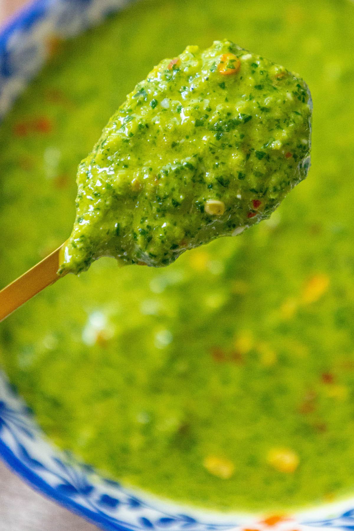 bright green zhoug sauce with flecks of cilantro and red pepper flakes in a decorative blue mug