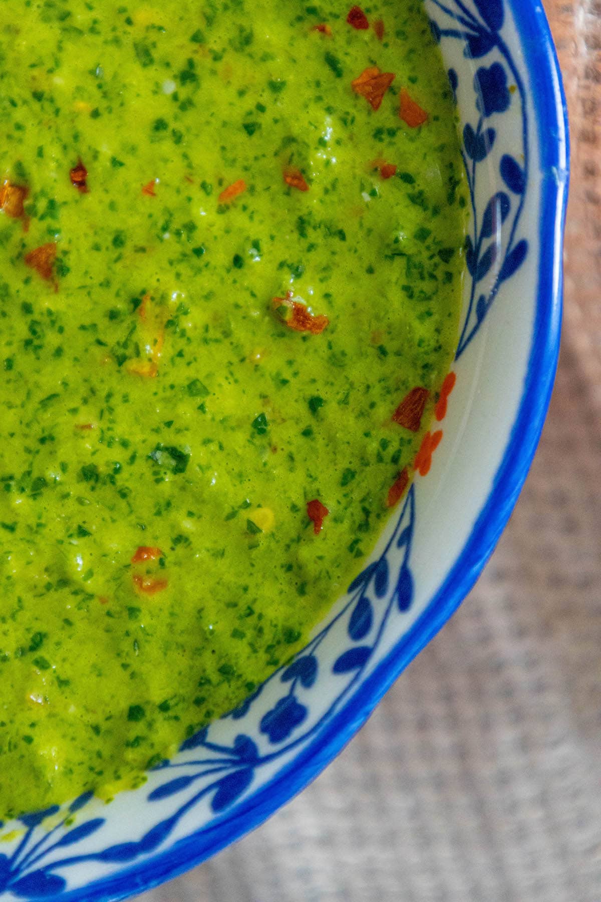 bright green zhoug sauce with flecks of cilantro and red pepper flakes in a decorative blue mug