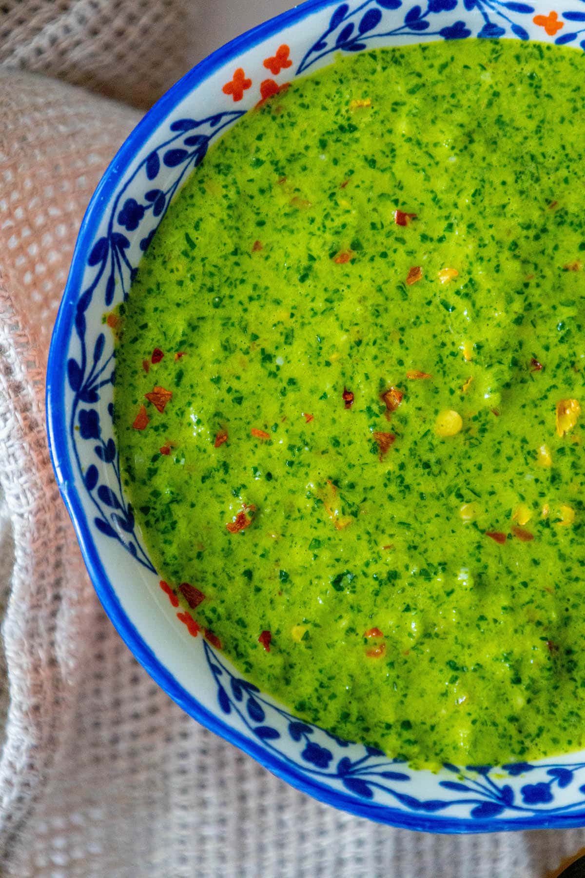 bright green zhoug sauce with flecks of cilantro and red pepper flakes in a decorative blue mug