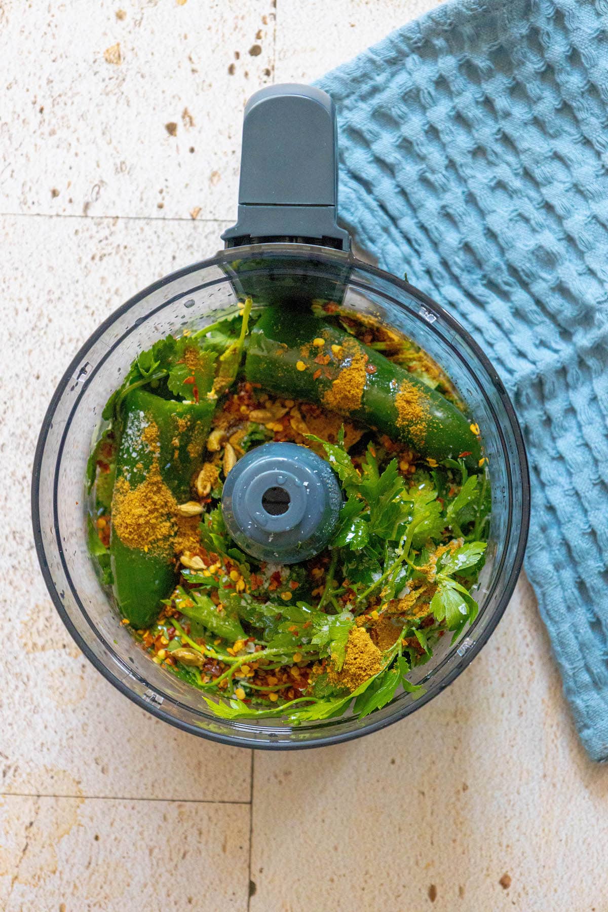 A food processor filled with vegetables and [Israeli cilantro zhoug sauce].