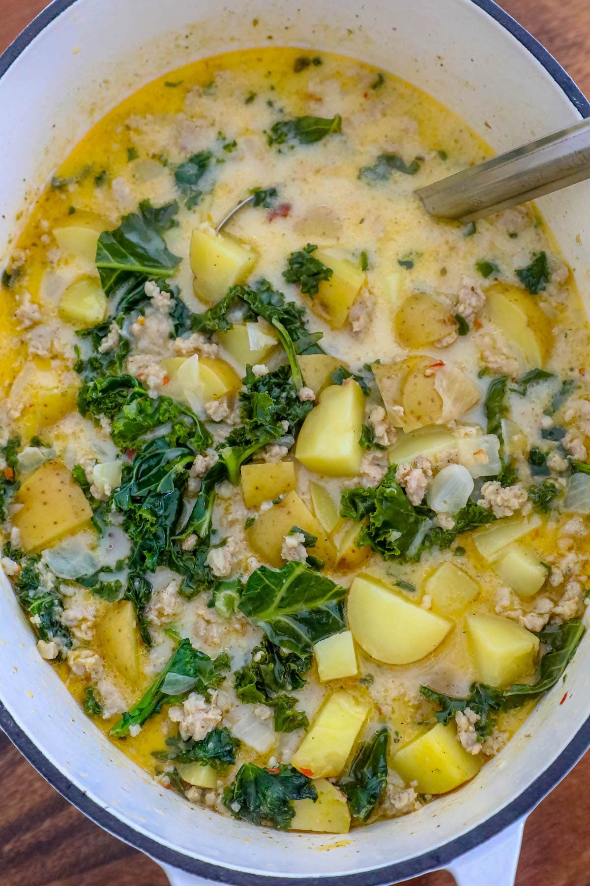 zuppa toscana soup with kale, potatoes, cream, and sausage in a white dutch oven with a ladle in it