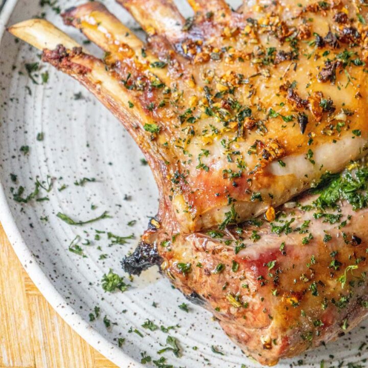 roasted rack of lamb with garlic and herb crust on a white speckled plate on a table