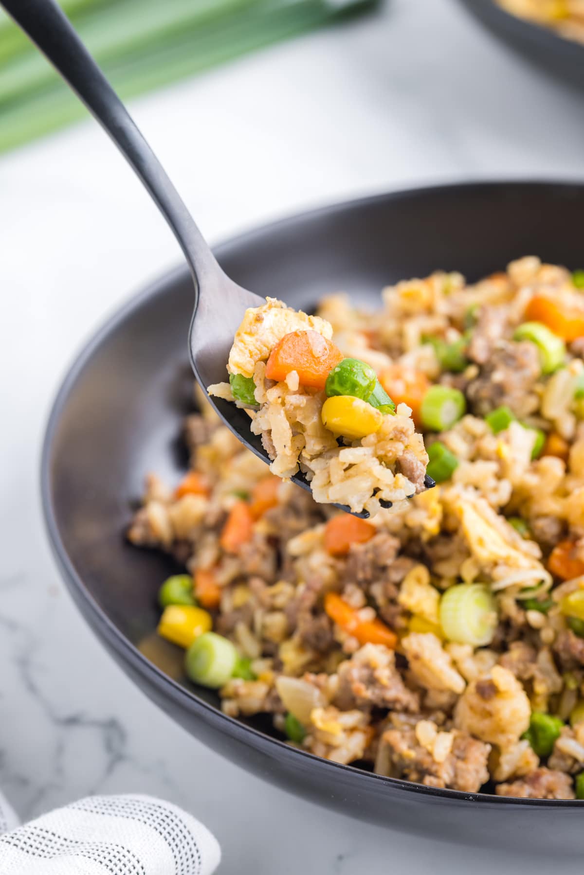 ground beef fried rice with carrots, peas, corn, and green onions on a spoon