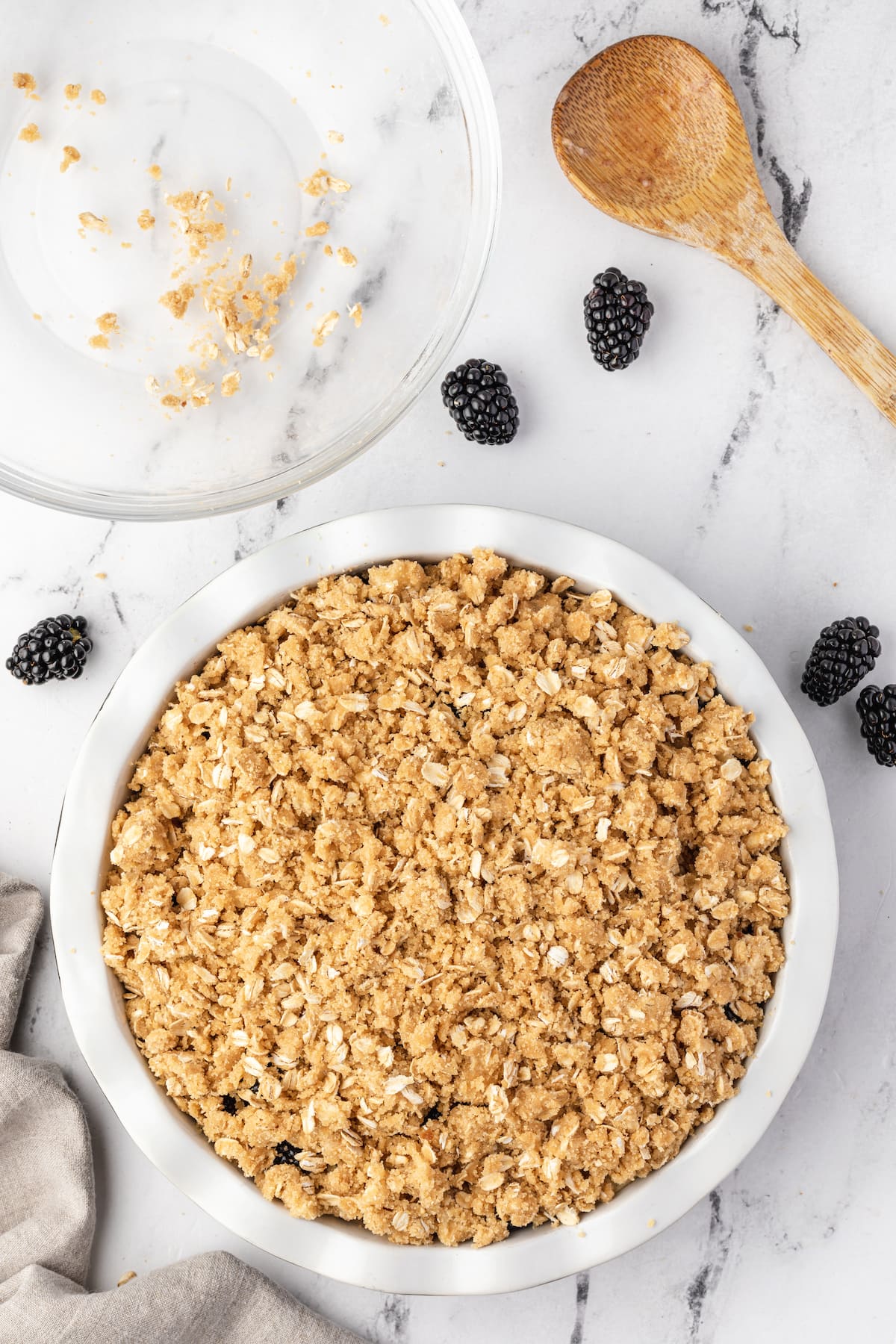 Blackberry granola in a white bowl next to a wooden spoon with apple crumble.