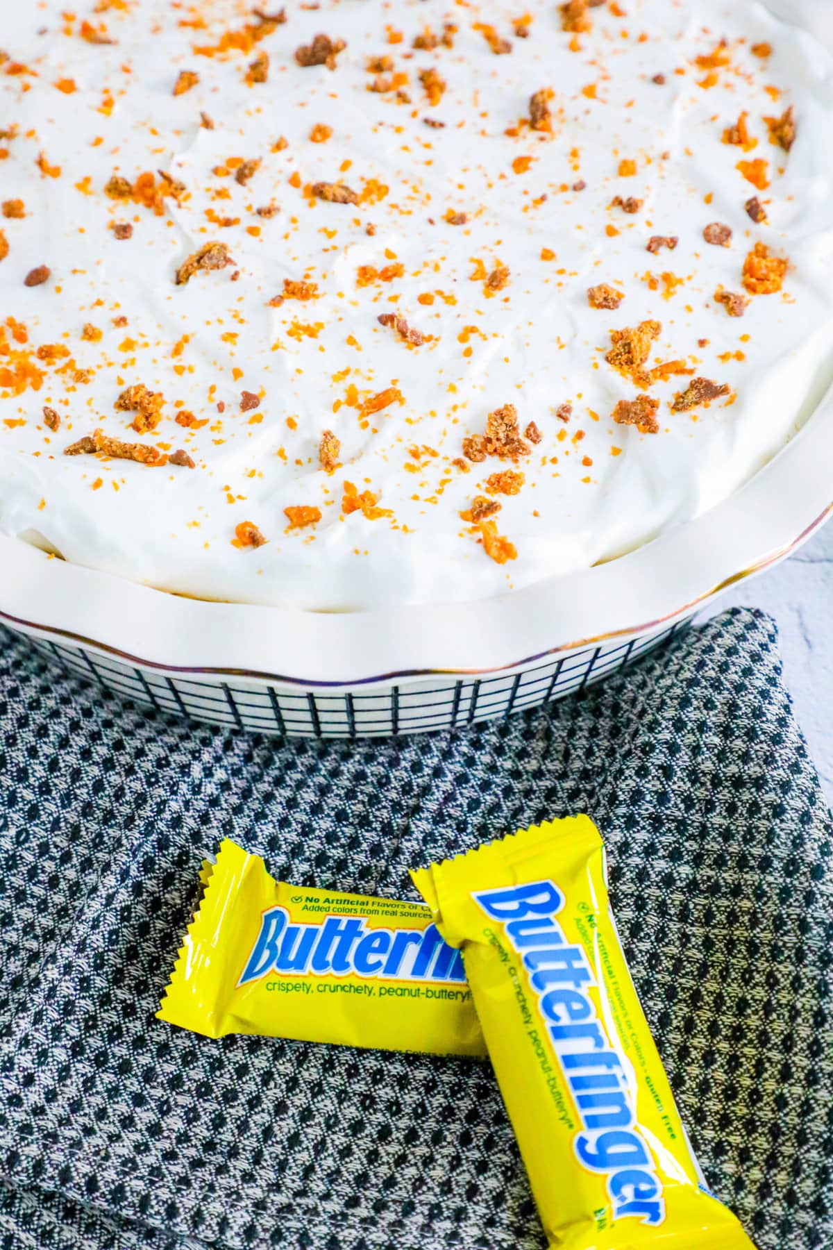 no bake butterfinger cream pie with an oreo crust in a white pie plate on a table topped with butterfinger candy crumbles