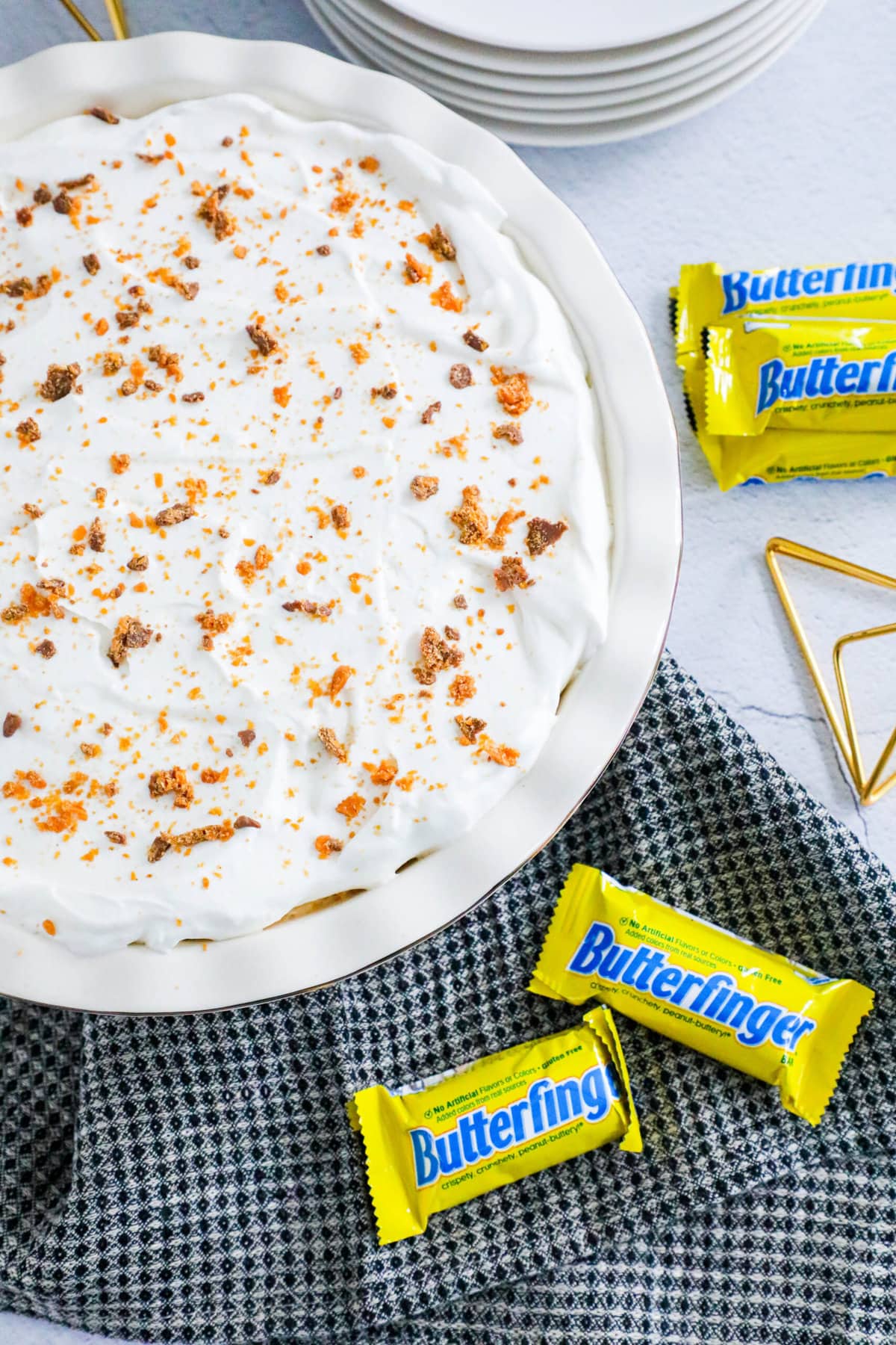 no bake butterfinger cream pie with an oreo crust in a white pie plate on a table topped with butterfinger candy crumbles