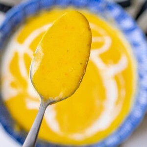 A spoon is holding a bowl of butternut squash soup.