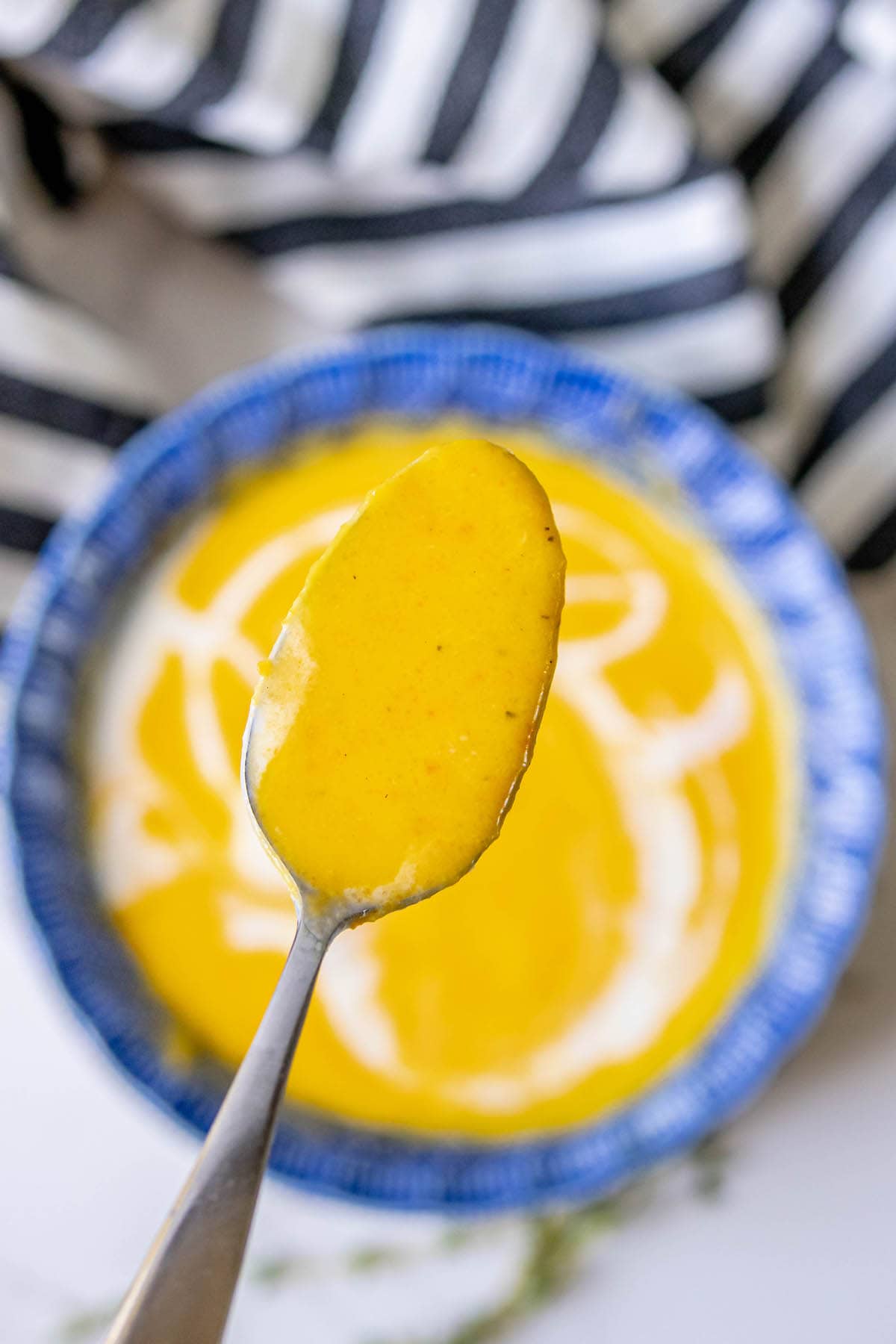 spoonful or orange soup with soup bowl in the background