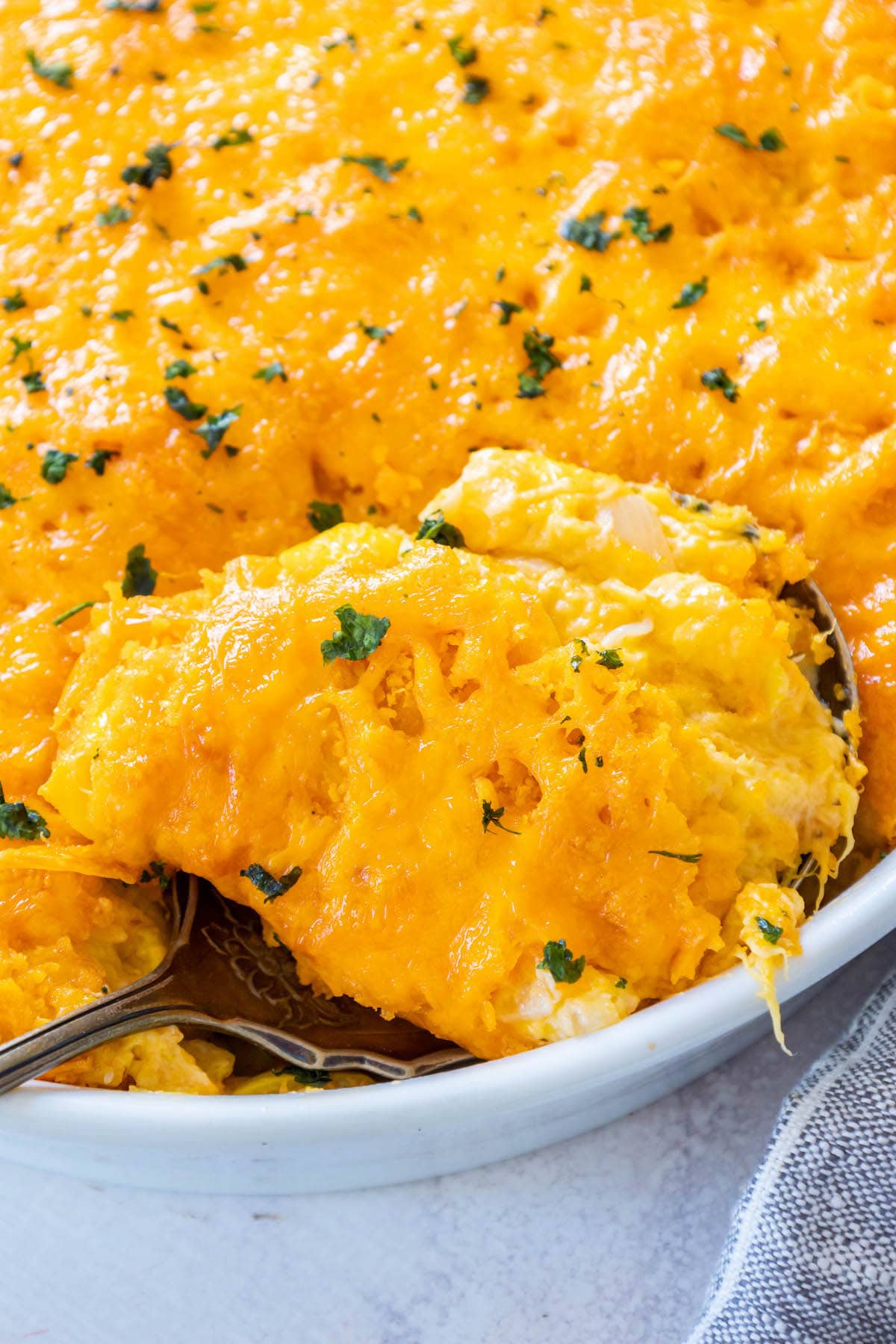 squash casserole baked in a white dish topped with cheese crackers and cheddar cheese and chopped parsley
