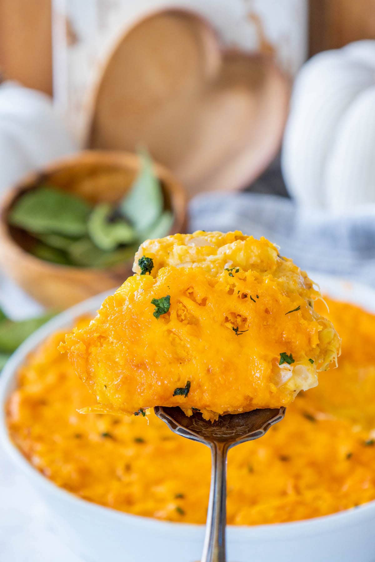 squash casserole baked in a white dish topped with cheese crackers and cheddar cheese and chopped parsley