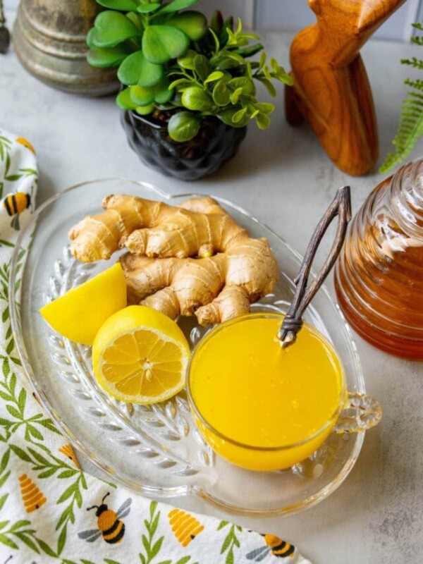 yellow tea in a glass cup with ginger, lemon, and honey in the background