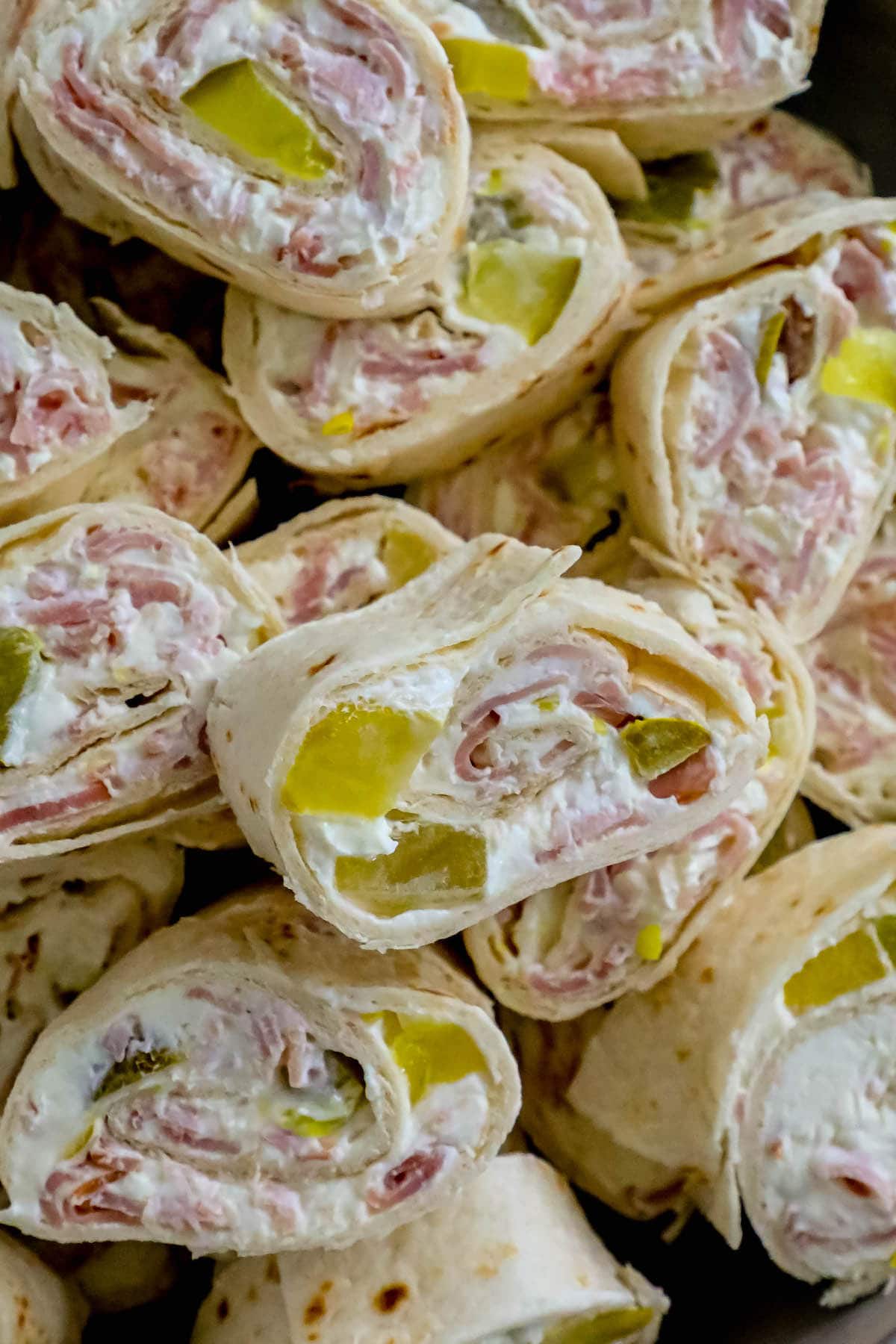 sliced pinwheel sandwiches in tortillas with cream cheese, ham, and pickles stacked in a metal bowl 