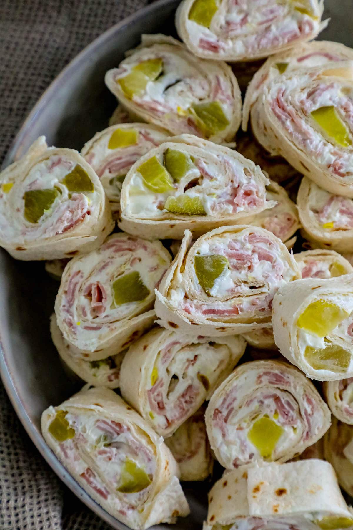sliced pinwheel sandwiches in tortillas with cream cheese, ham, and pickles stacked in a metal bowl 