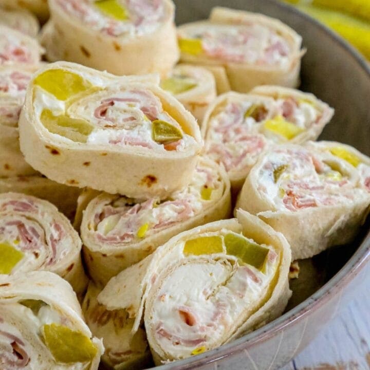 sliced pinwheel sandwiches in tortillas with cream cheese, ham, and pickles stacked in a metal bowl