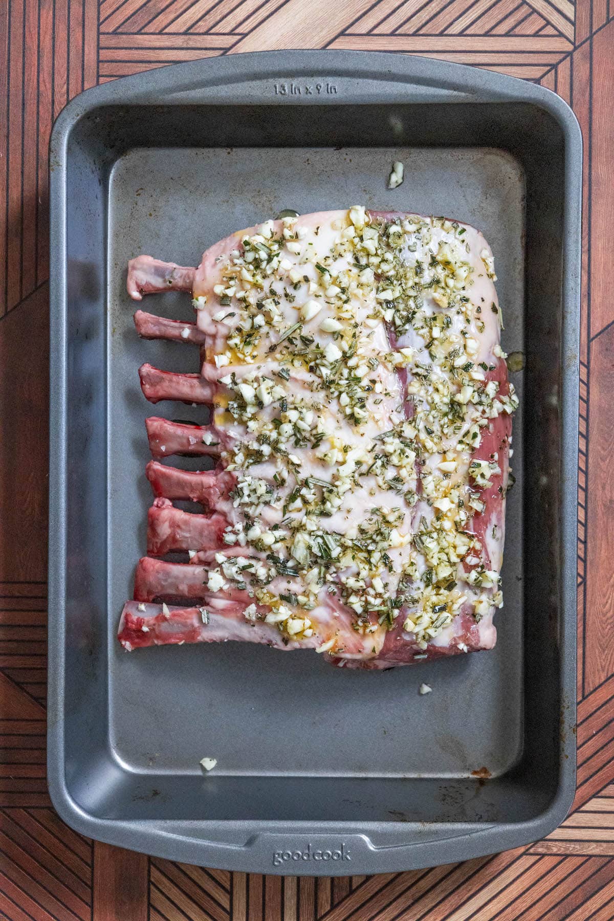 rack of lamb coated in herbs, olive oil, minced garlic in a roasting pan