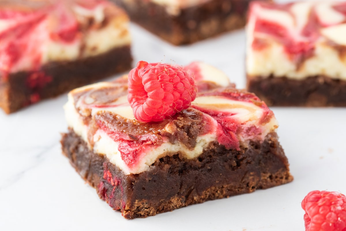 cheesecake marbled brownie bar with raspberry sauce and a raspberry on top