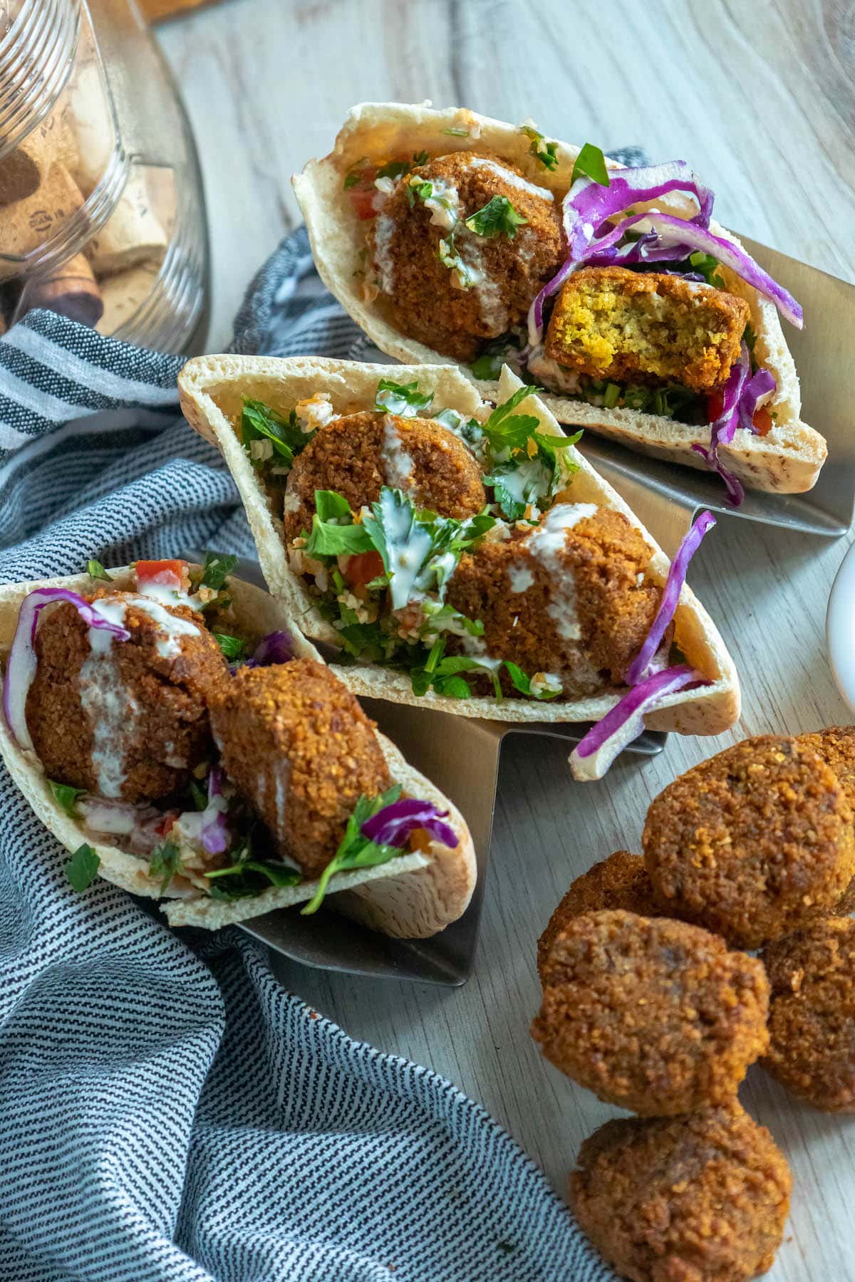 three pitas stuffed with falafel balls, cabbage, and salad with tahini sauce ladled on top