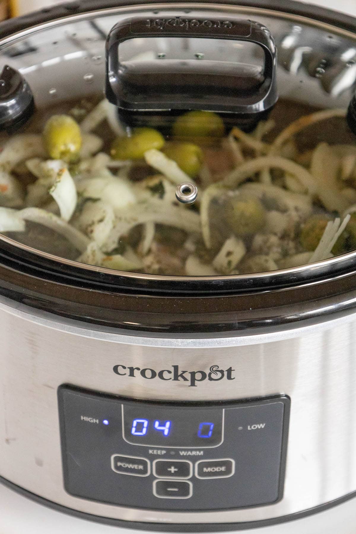 The slow cooker with Greek-style pork chops, covered and cooking, promising a tender and flavorful meal.
