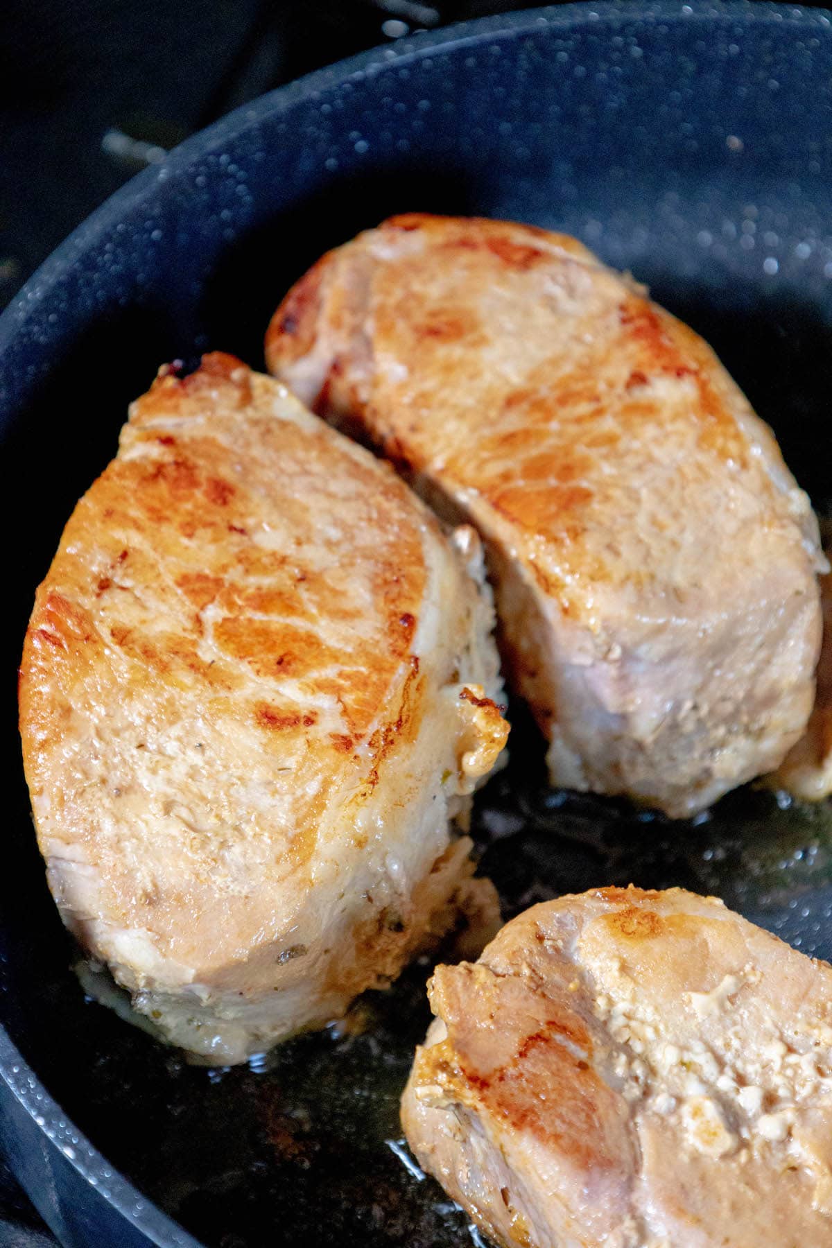 Pork chops beautifully browning in a hot skillet, creating a perfect crust before slow cooking.