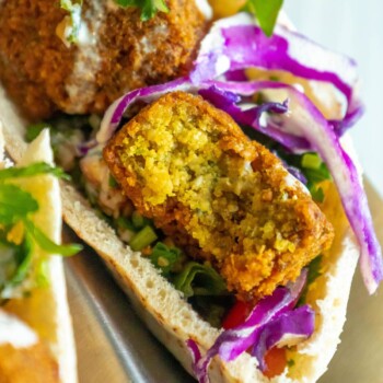 three pitas stuffed with falafel balls, cabbage, and salad with tahini sauce ladled on top