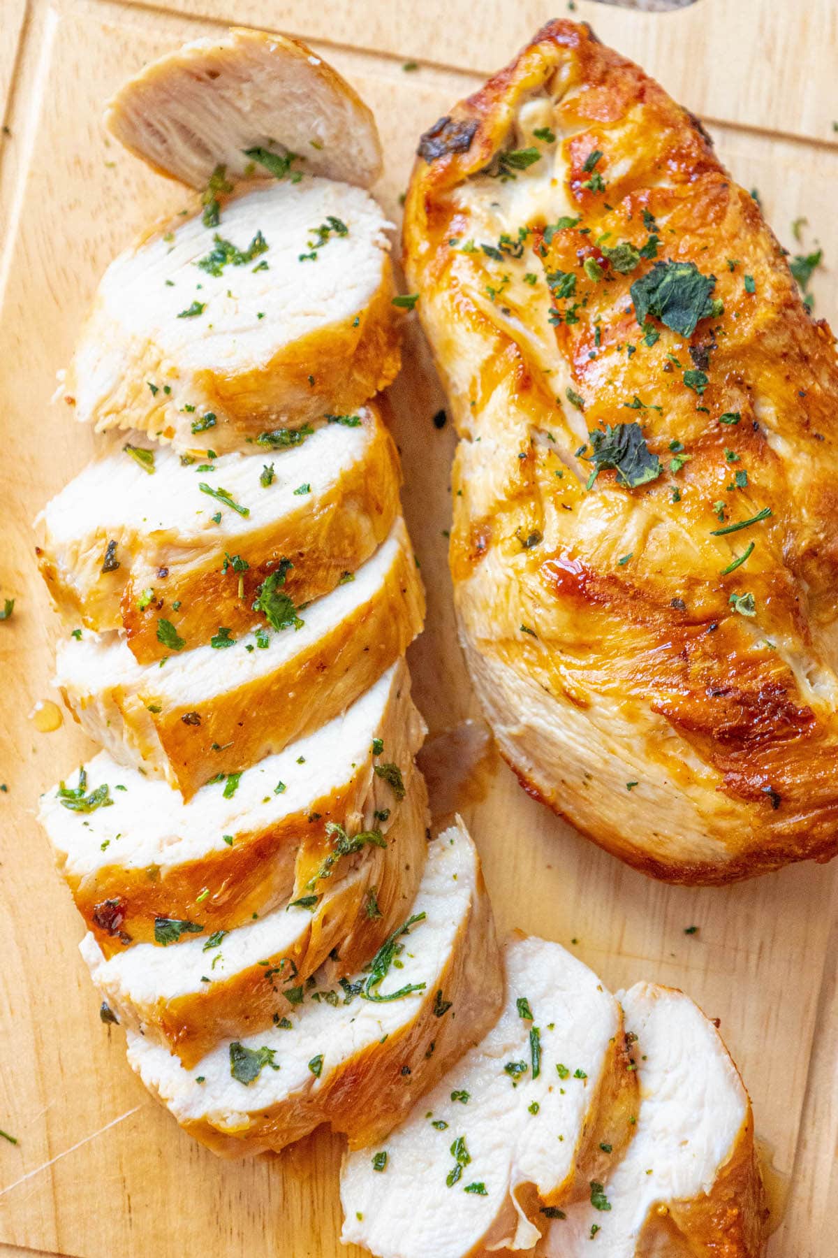 sliced grilled chicken breast on a cutting board with chopped parsley on top