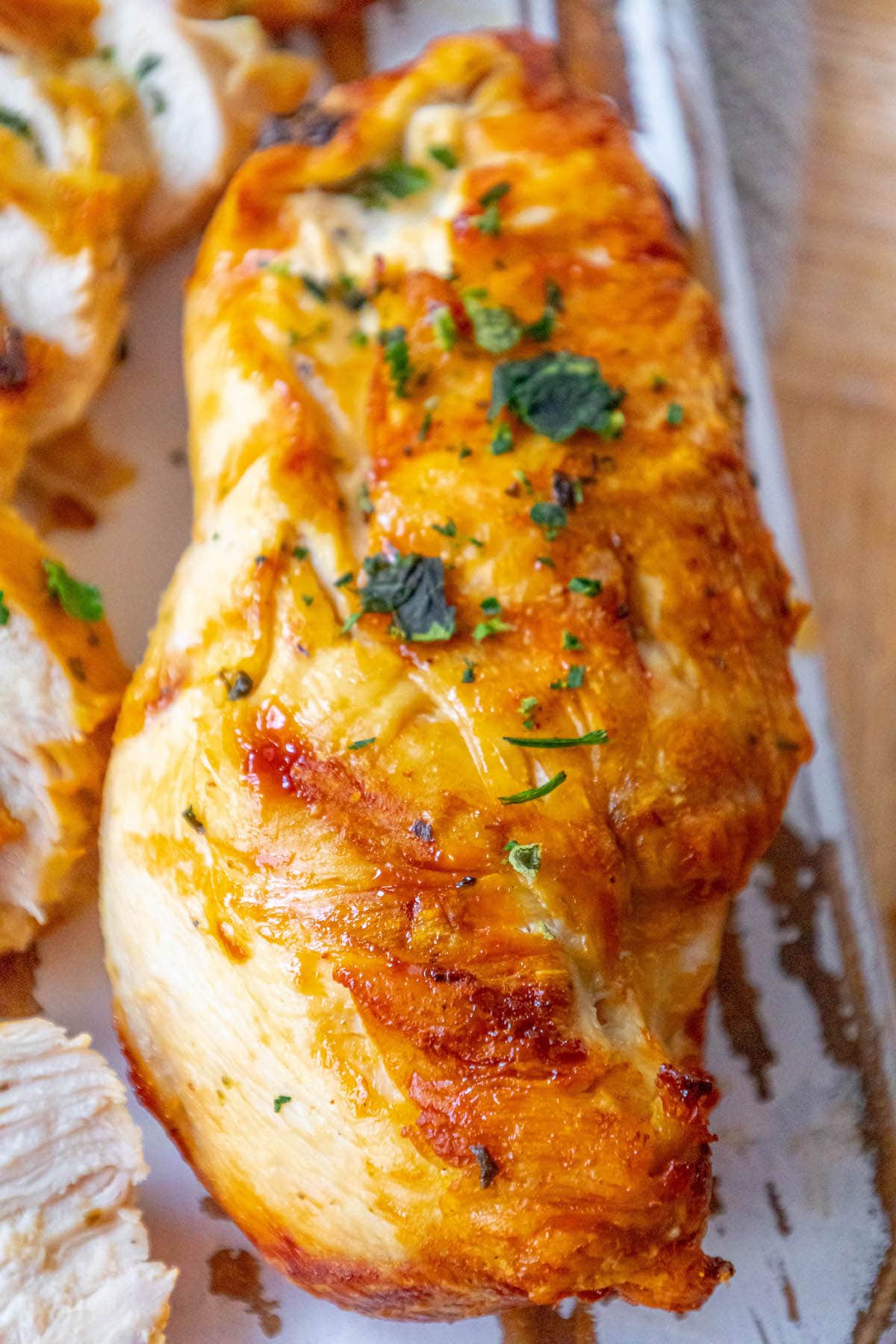 grilled chicken breast with chopped parsley on top on a white cutting board