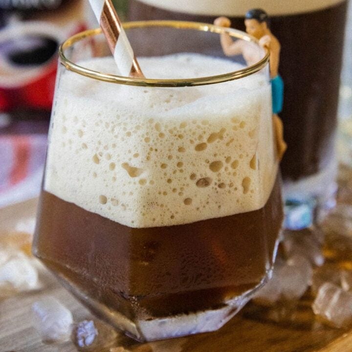 whipped Greek frappé coffee in a glass with ice and foam and a paper straw on a table
