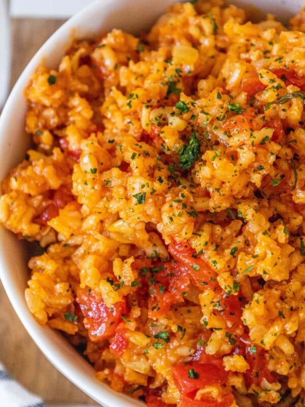 red rice with chunks of tomatoes and chopped cilantro in a white bowl on a table
