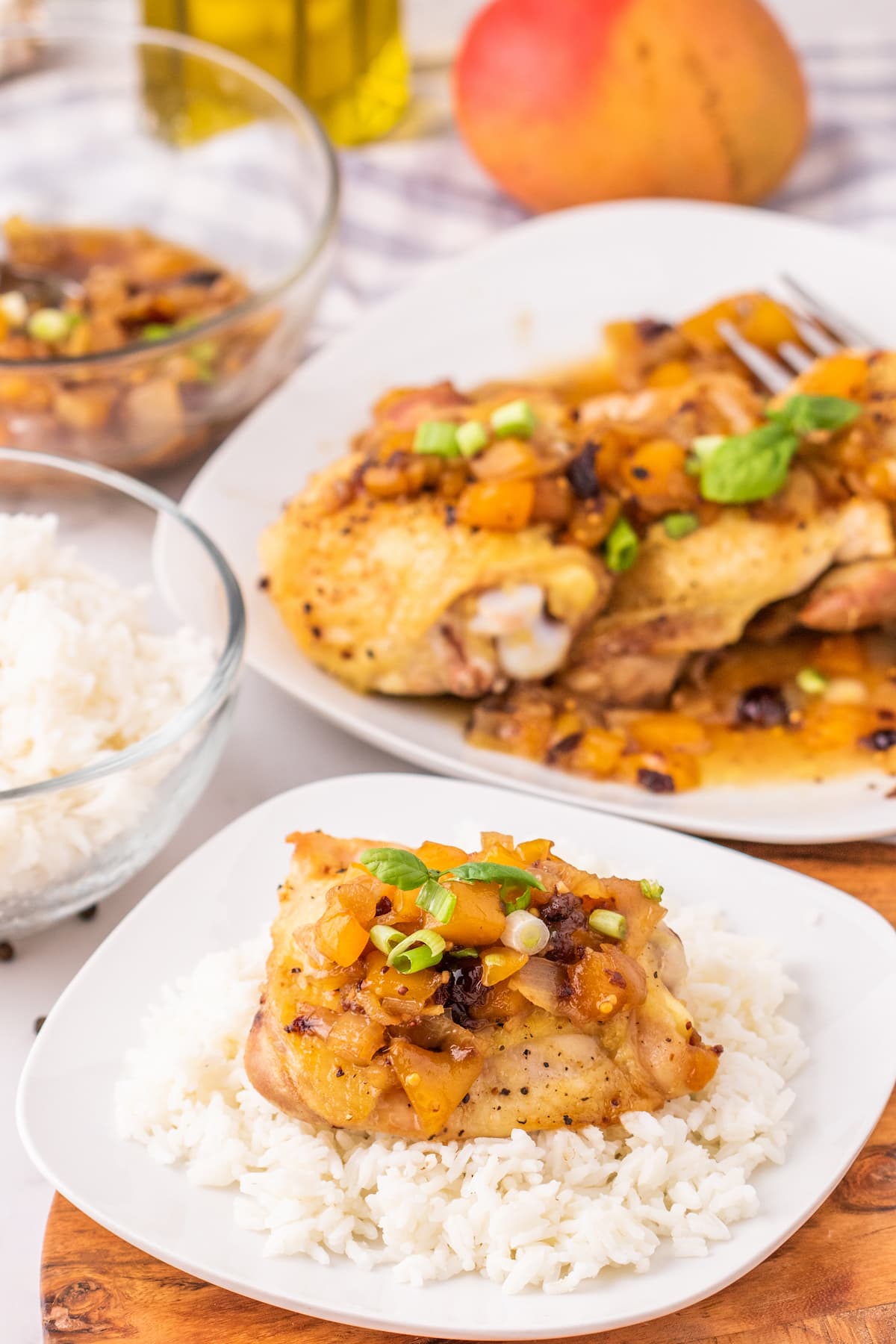 baked chicken thigh on a white plate covered in mango chutney and sliced green onions