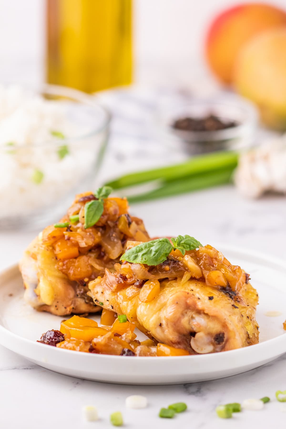 baked chicken thigh on a white plate covered in mango chutney and sliced green onions