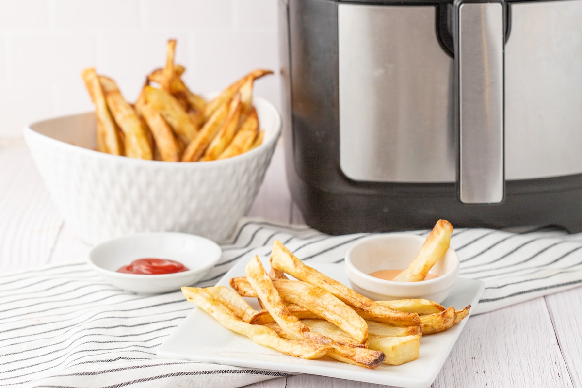 crispy air fried french fries on a white plate in front of fry sauce and an air fryer on a table