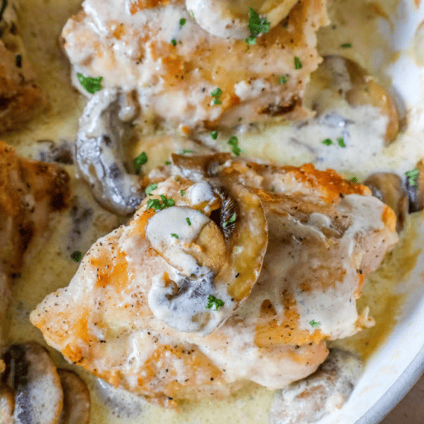 Chicken breasts cooked with mushrooms and cream sauce in a skillet, creating a creamy and indulgent dish.