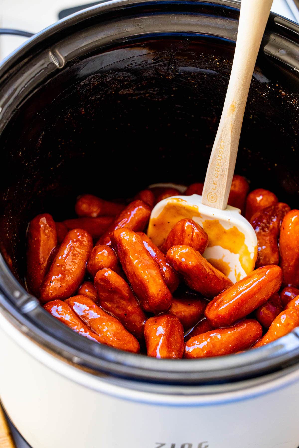 little smokies in bbq sauce in a crock pot with a spatula in the middle