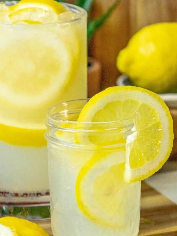 lemonade in a glass jar with a slice of lemon on the side and pebble ice in the glass