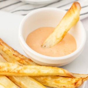 french fry being dipped into a small cup of fry sauce