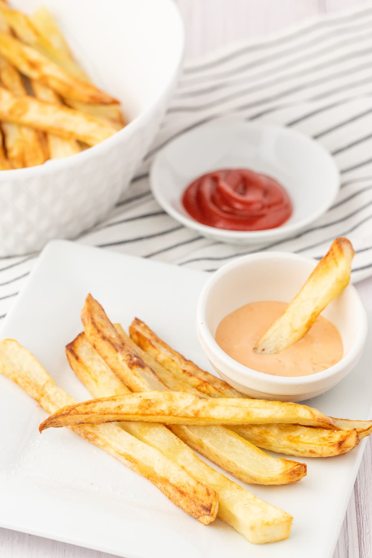 french fries on a plate next to a french fry being dipped into a small cup of fry sauce