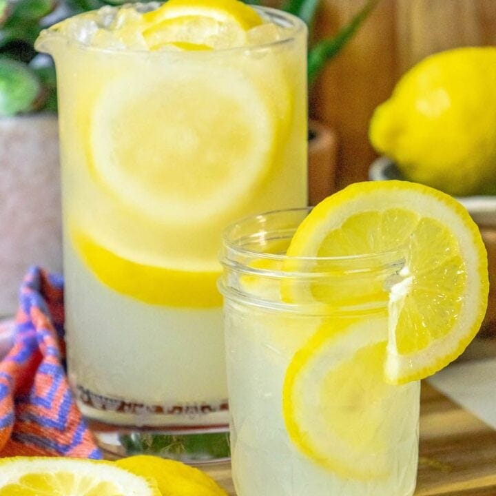 lemonade in a glass jar with a slice of lemon on the side and pebble ice in the glass