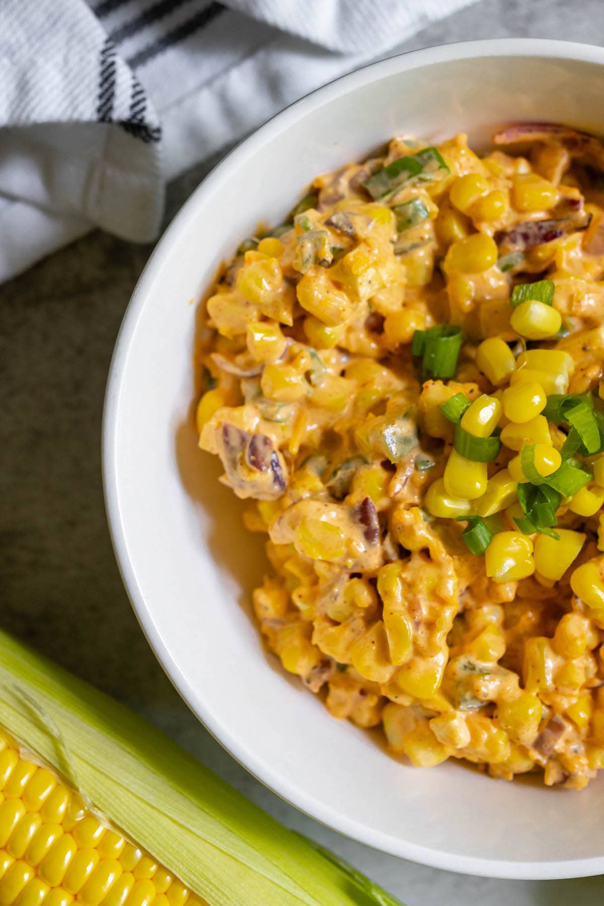 creamy corn salad with jalapeños, corn kernels, diced green onion, and cheese in a white bowl
