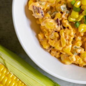 creamy corn salad with jalapeños, corn kernels, diced green onion, and cheese in a white bowl
