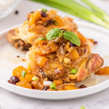 baked chicken thigh on a white plate covered in mango chutney and sliced green onions