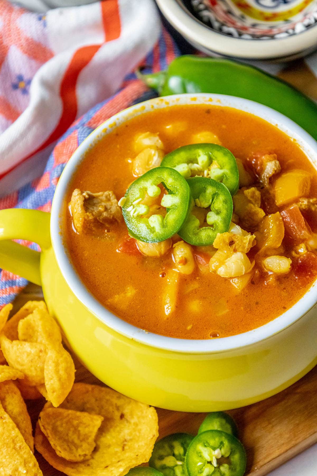 Red posole made with pork shoulder, hominy, and a blend of spices topped with jalapenos in a bowl