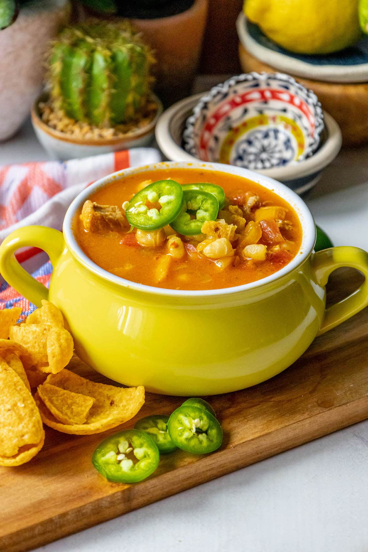 Red posole made with pork shoulder, hominy, and a blend of spices topped with jalapenos in a bowl