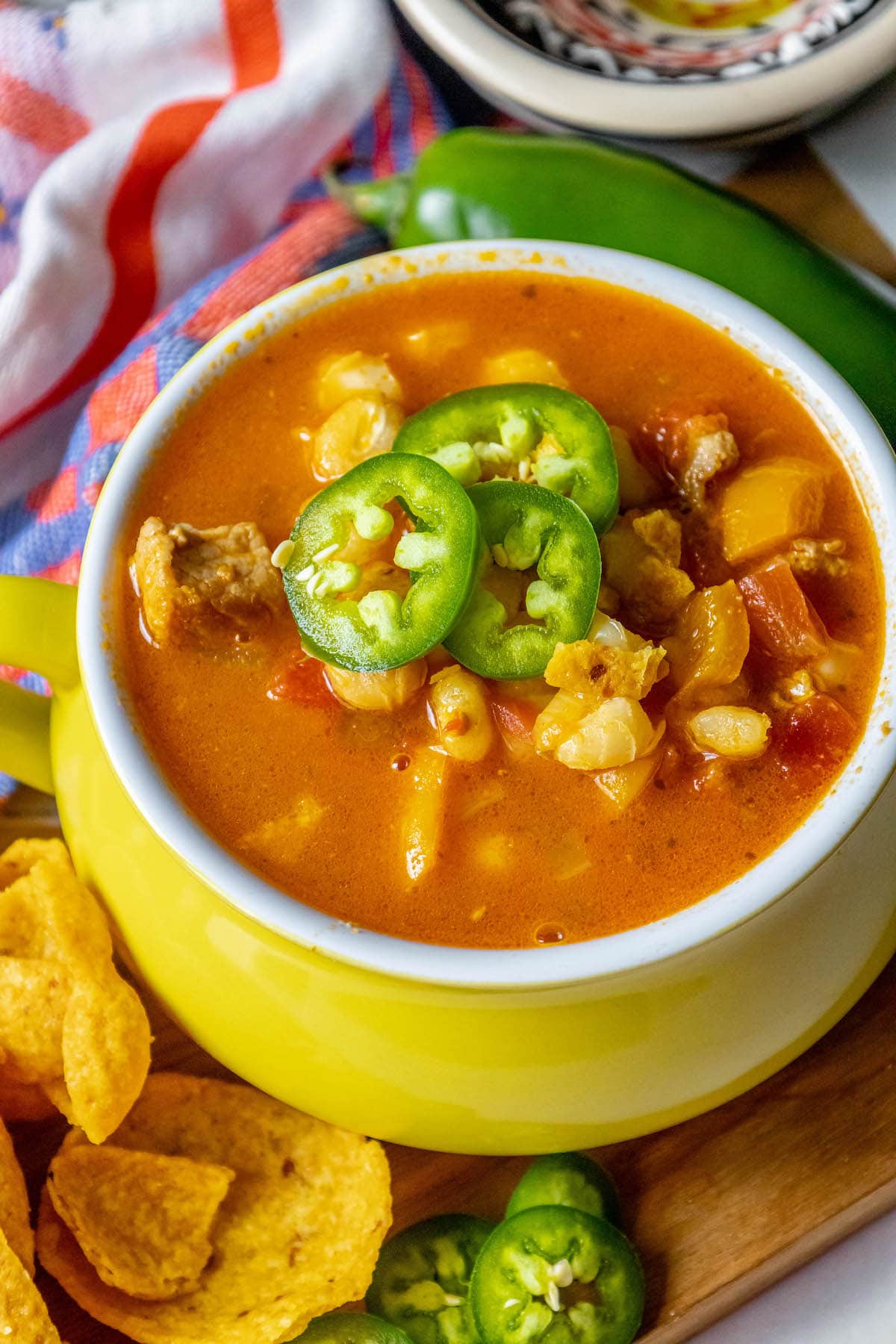 Red posole made with pork shoulder, hominy, and a blend of spices topped with jalapenos in a bowl