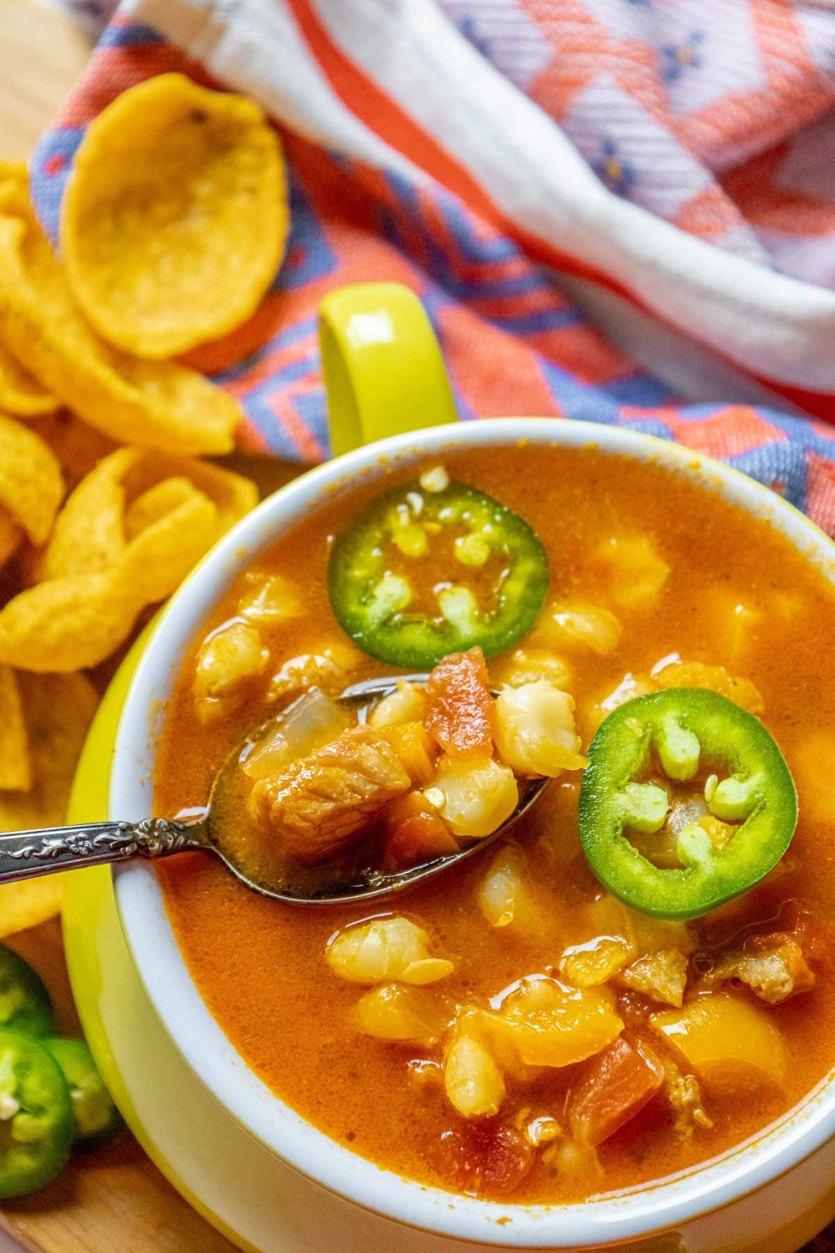 Red posole made with pork shoulder, hominy, and a blend of spices topped with jalapenos in a bowl