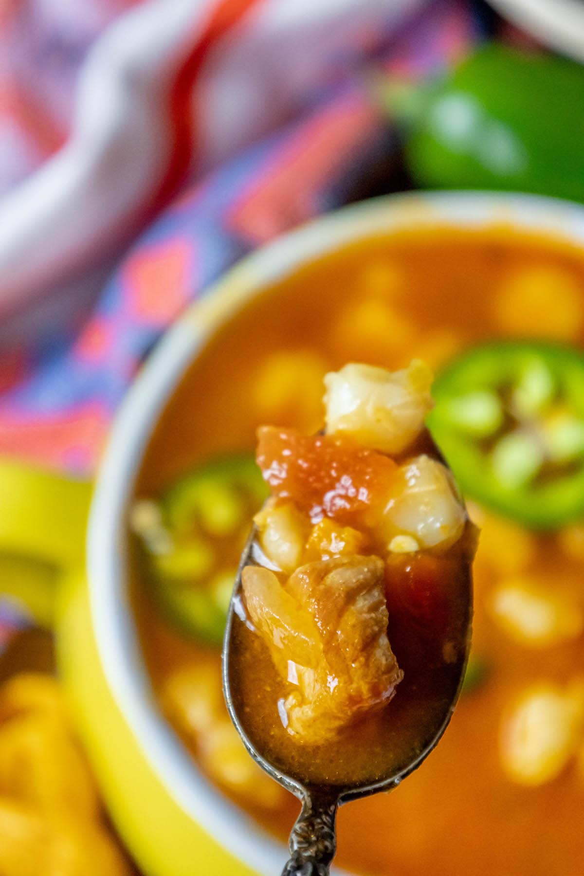 Red posole made with pork shoulder, hominy, and a blend of spices topped with jalapenos in a bowl