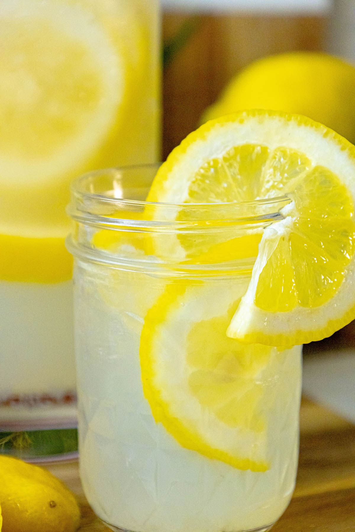 lemonade in a glass jar with a slice of lemon on the side and pebble ice in the glass