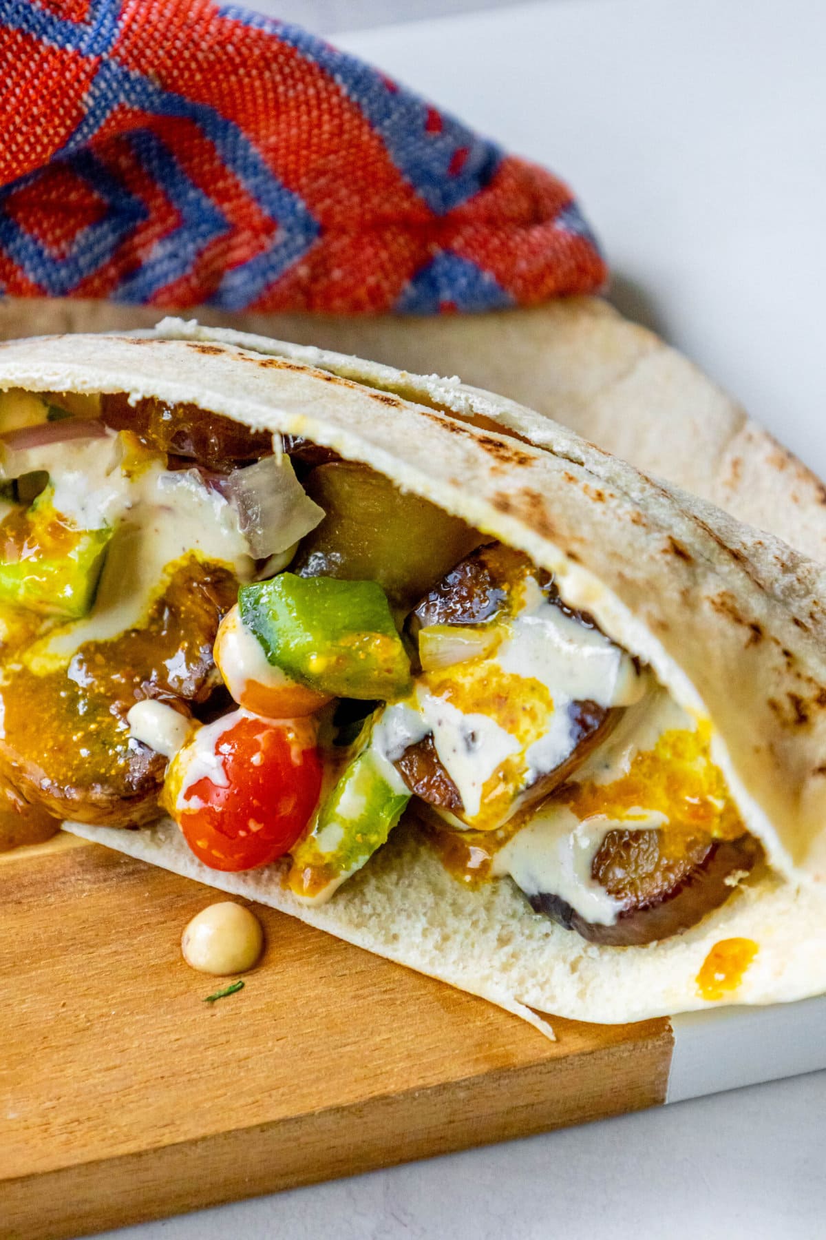A vegan sabich sandwich is resting on a wooden cutting board.