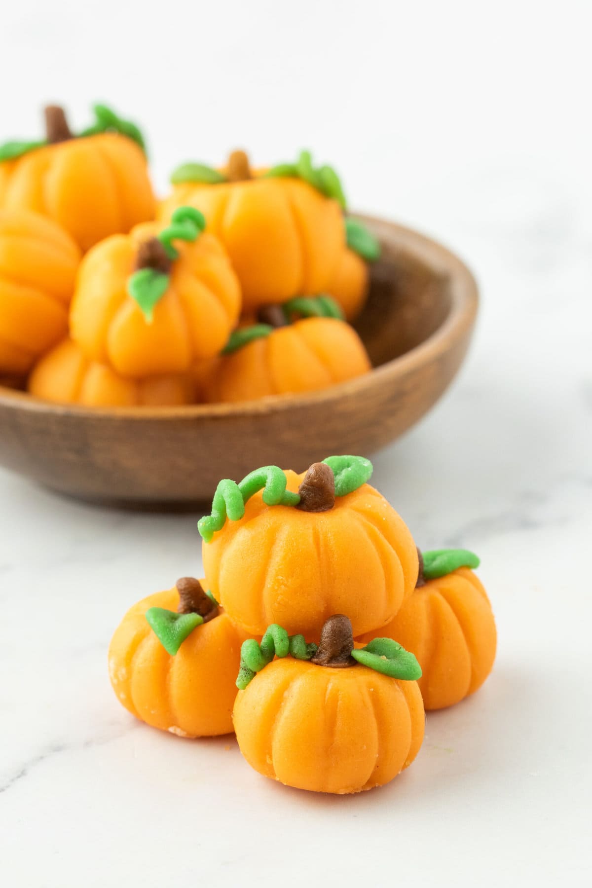Marzipan pumpkin candies in a bowl on a marble table.
