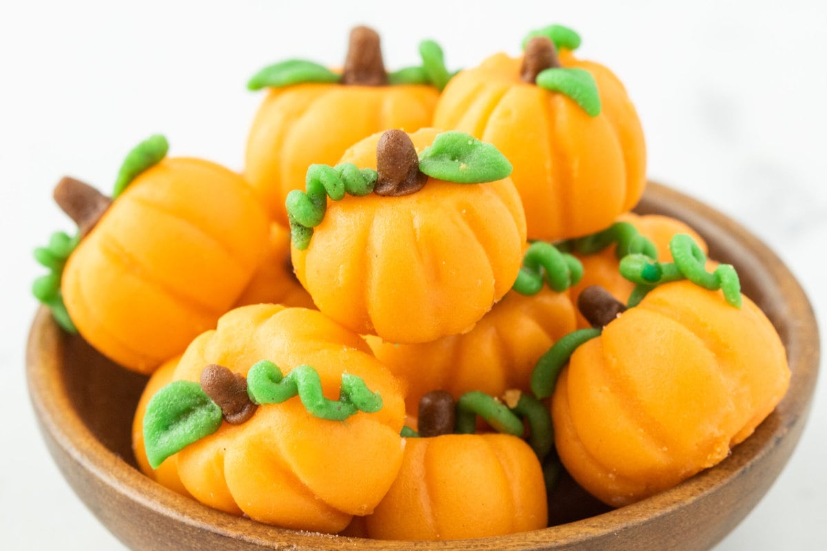 marzipan pumpkins with stem and leaf stacked in a bowl