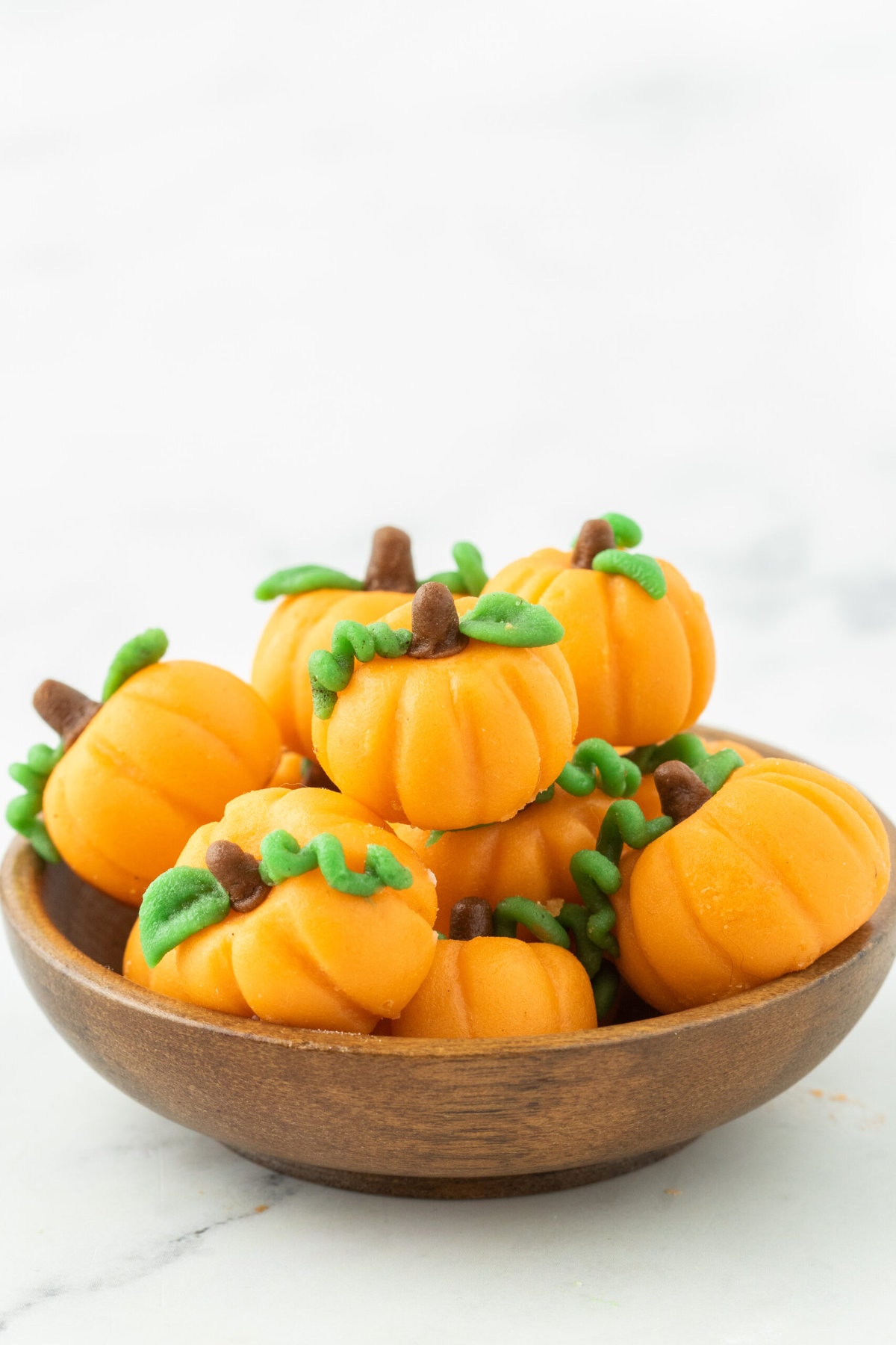 marzipan pumpkin with stem and leaf stacked in a bowl